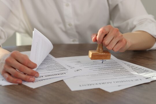 Woman stamping licensing agreement document at wooden table indoors, closeup