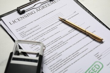 Licensing agreement document, pen and stamp on white table, closeup