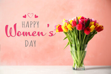 Happy Women's day card. Glass vase with beautiful bright tulips on table against coral background