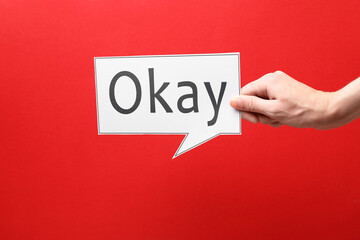 Woman holding paper speech bubble with word Okay on red background, closeup