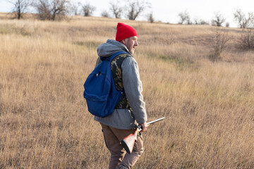Mature hunter man holding a shotgun and walking through a field