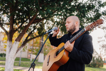 Fototapeta premium Street musician singing and playing acoustic guitar in park