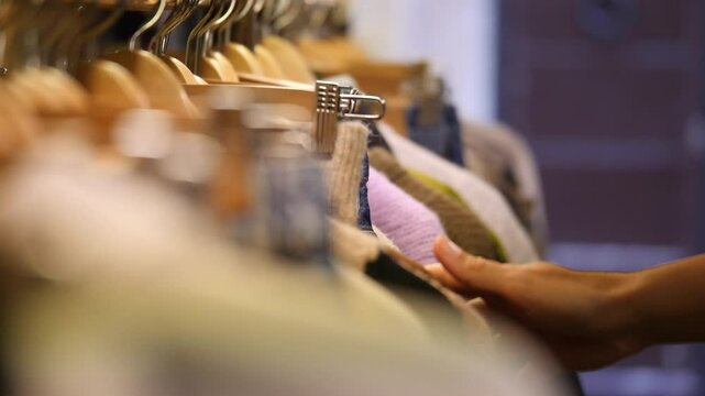 Donna sceglie degli abiti in un negozio di abbigliamento. 
Abiti appesi sulle stampelle in un centro commerciale. Primo piano della mano sui prodotti.