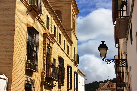 Old brick building with black wrought iron balconies and window grilles; ornate street lamp attached to the wall; blue sky with white clouds in the background;