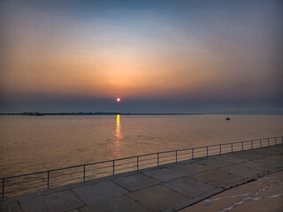 A beautiful sunset casts vibrant hues over a calm waterfront, creating a serene atmosphere. the sun sets on the horizon, reflecting on the water and illuminating the sky with warm colors. the peaceful