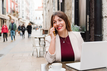 Businesswoman working remotely from a cafe, talking on phone and smiling