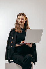 Young successful business woman in black suit working with laptop at studio on white background