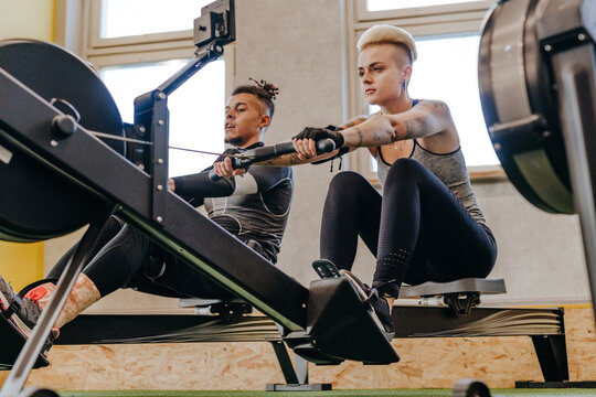 Athlete man and woman performing exercises with rowing machine