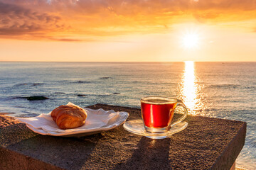 concept of street outdoor breakfast with a cup of tea or coffee on a morning coast during sunrise. landscape of city embarkment with sea water and cloudy sky on background