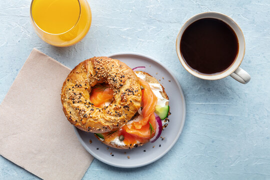 Lox bagel. A breakfast of a sandwich with smoked salmon and fresh vegetables on a plate, with orange juice and coffee, shot from the top - Powered by Adobe