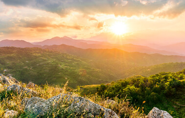 highland mountain landscape of beautiful sunset or sunrise with nice mountain peaks and slopes, green and golden hills and majestic cloudy sky on background