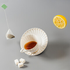 Floating tea bag, lemon and white porcelain cup with tea on grey background. Creative tea drinking image