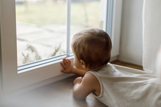 Cute baby at window close up. Adorable infant playing with window glass. Baby activity and baby proofing