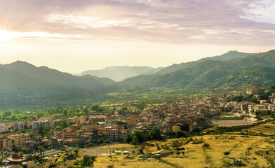 Obraz premium amazing mountain landscape with old yellow italian town among green beatiful mountains and cloudy sky above