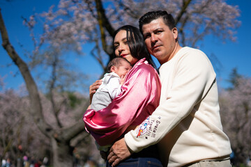 Happy latin parents holding newborn baby in blooming park