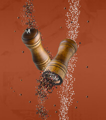 Salt and pepper mills in air on dark orange background
