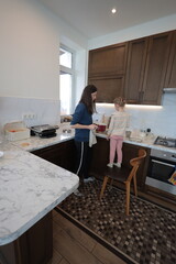 Mother and a child girl cooking and eating indoors together 