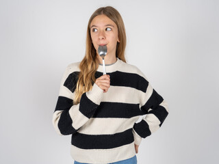 Very hungry beautiful caucasian teen girl wearing striped sweater holding spoon into mouth dream of...