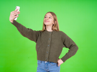 beautiful caucasian girl wearing green sweater smiling and taking a selfie ready to post it on her...