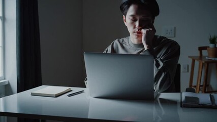 A frustrated or disappointed person sitting in a dark room, staring at a laptop screen showing an empty email inbox.