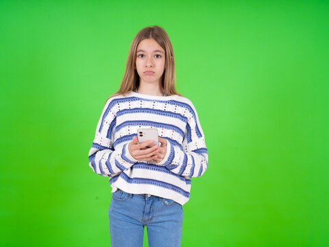 Upset dissatisfied beautiful caucasian girl wearing striped sweater uses mobile software application and surfs information in internet, holds modern mobile hand