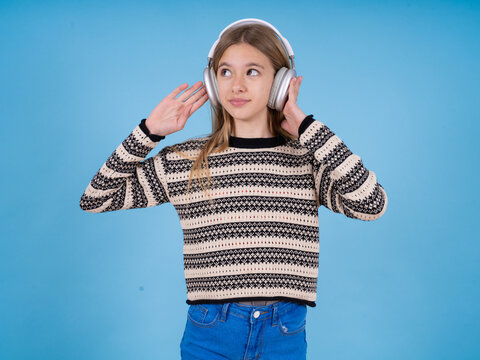 Joyful beautiful caucasian girl wearing striped sweater sings song keeps hand near mouth as if microphone listens favorite playlist via headphones