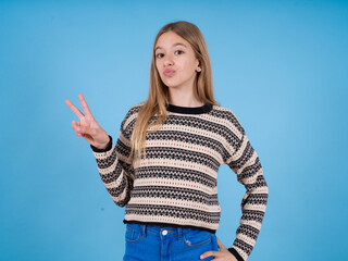 beautiful caucasian girl wearing striped sweater makes peace gesture keeps lips folded shows v sign. Body language concept