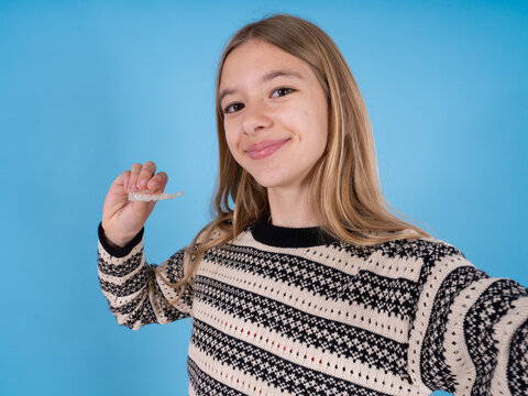 beautiful caucasian girl wearing striped sweater make selfie holding an invisible braces aligner, recommending this new treatment. Dental healthcare concept.