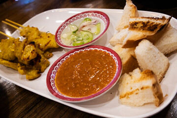 Thai food fusion style cuisine grilled Moo Satay or roasted pork satay with peanut sauce amd side dish pickles cucumber slices onions in vinegar with bake bread of cafe restaurant in Bangkok, Thailand