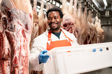 Experienced butcher holding basket full of chopped meat in slaughterhouse.