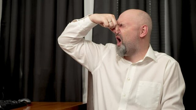 Man covering nose with hand, grimacing and burping from bad smell. Man holding nose with hand, making face and belching due to stink. Guy pinching nose, wincing and gagging from awful odor