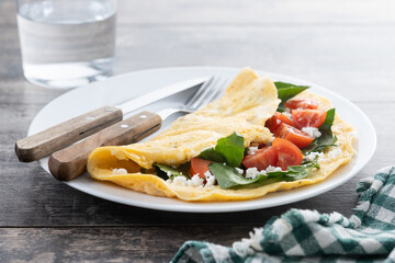 Stuffed omelette with tomatoes and spinach on wooden table