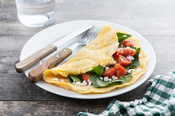 Stuffed omelette with tomatoes and spinach on wooden table
