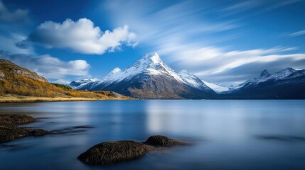 Obraz premium Majestic Snow-Capped Mountain Reflected in Calm Lake Under a Bright Blue Sky with Fluffy White Clouds