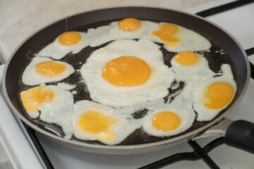 Chicken egg and 9 quail eggs in frying pan.