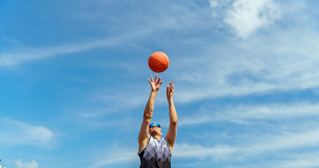 Athlete shooting a basketball under a bright blue sky during a sunlit afternoon practice session