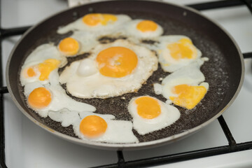 Chicken egg and 9 quail eggs in frying pan.
