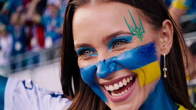 Smiling Ukrainian sports fan with vibrant flag face paint at a stadium event  
