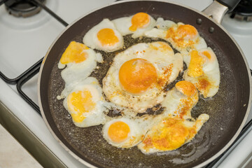 Chicken egg and 9 quail eggs in frying pan.