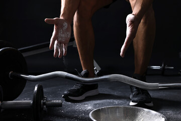 Obraz premium Man applying talcum powder onto his hands before training with barbell on black background, closeup