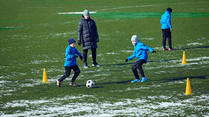 Group of young athletes engaged in active football drill, coach directing movement, cold outdoor practice. Passion and hard work. Concept of development, sport, motivation, teamwork, growth.