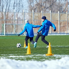 Obraz premium Youth players reacting quickly, improving decision-making and ball control on snowy green field. Focus and agility. Concept of sport, training, perseverance, dynamic movement, ambition.