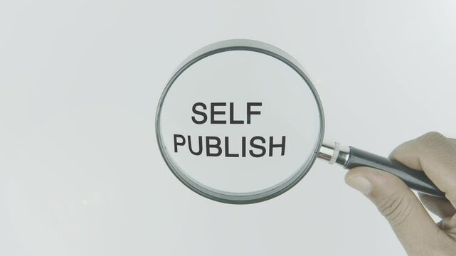 Self publish text or word highlighted by a magnifying glass in a hand on a white background, symbolizing focus on independent publishing, creative control, and personal authorship