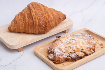 almond croissants on wooden cutting board on white marble background