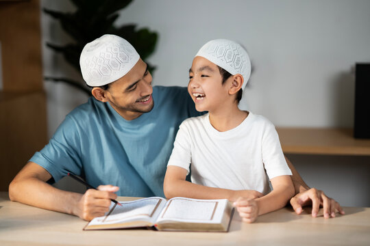 Muslim father and son in mosque praying and reading holly book Quran together. Happy learning Islamic education concept. A man pround with hiis boy, sharing laugh and smile.