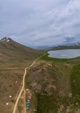Aerial view of serene Deosai Plains with mountains, a lake, and tents, Gilgit Baltistan, Pakistan.