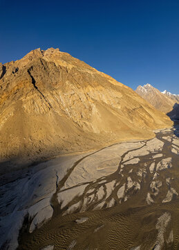Aerial view of majestic mountains and a vast valley with a dry riverbed under a clear sky, enroute K2 Trek - Jhola campsite, Gilgit Baltistan, Pakistan.
