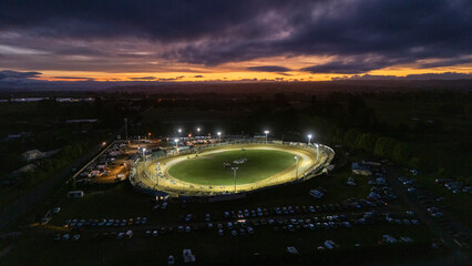 Aerial view of vibrant motor racing speedway under twilight with illuminated cars and enthusiastic crowd, Richmond, Tasman, New Zealand.