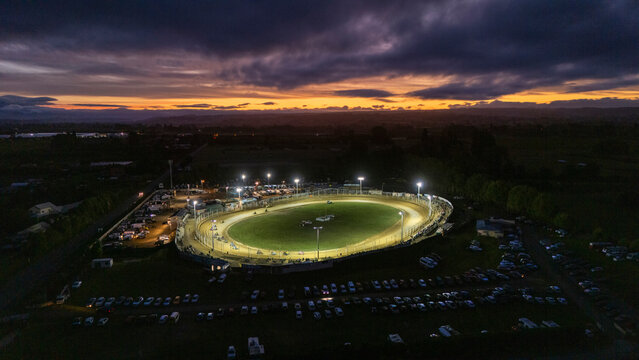 Aerial view of vibrant motor racing speedway under twilight with illuminated cars and enthusiastic crowd, Richmond, Tasman, New Zealand.