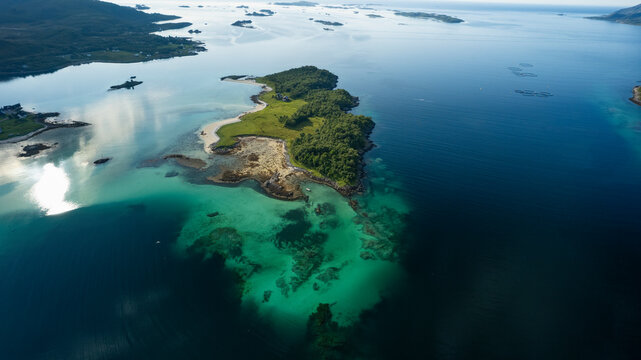 Aerial view of panoramic salmon farm on lush island surrounded by clear water and serene coastline, Kamoyvaer, Mageroy island, Finnmark, Norway.